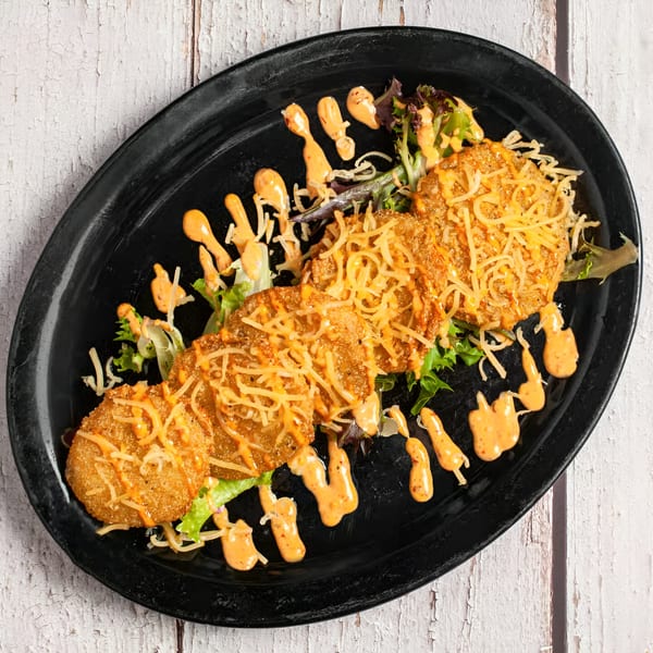 Fried green tomatoes with shredded cheese, lettuce, and a creamy orange sauce on a black plate.