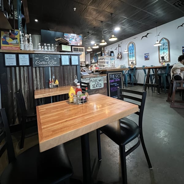 Interior of True Grit American Bistro, showing wooden tables, black chairs, and a coffee bar.