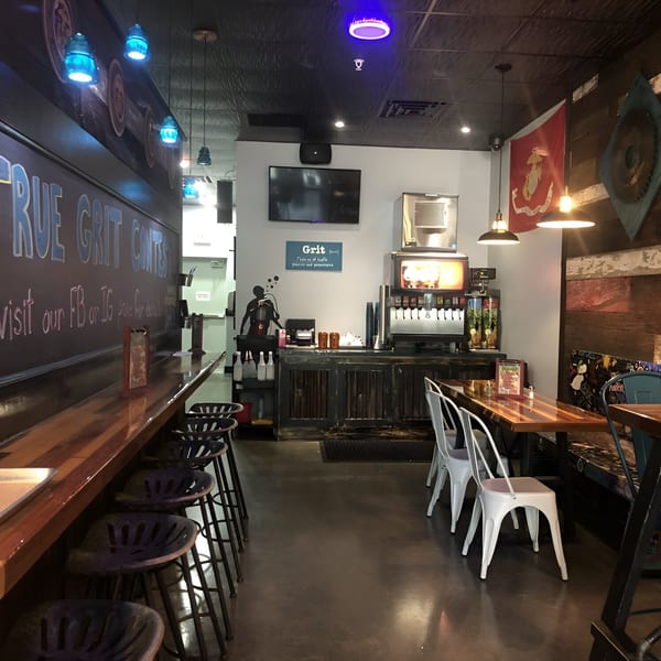 Interior of True Grit American Bistro with a long bar, stools, tables, and a drink station.