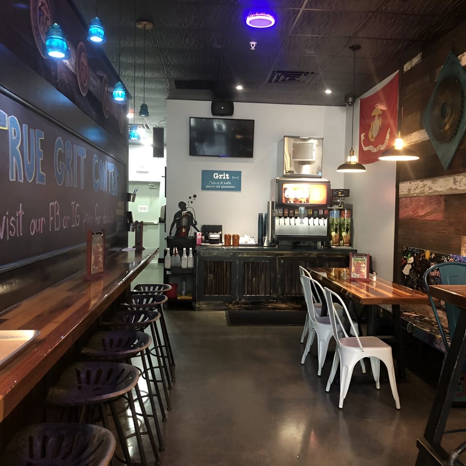 Interior of True Grit American Bistro with a long bar, stools, tables, and a drink station.
