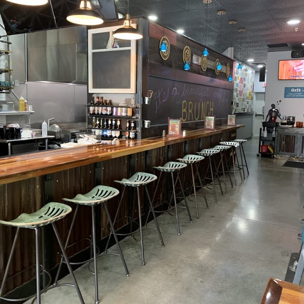 True Grit American Bistro's empty breakfast bar with green tractor-seat stools and a "Brunch" chalkboard.