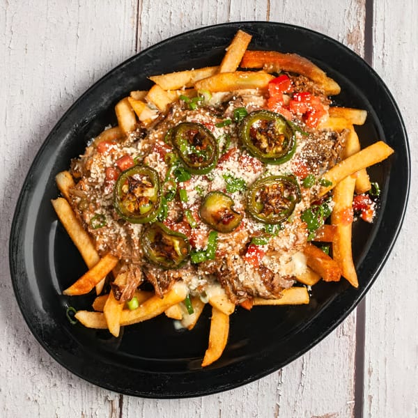 Loaded fries with shredded meat, melted cheese, diced tomatoes, jalapeños, and green onions.