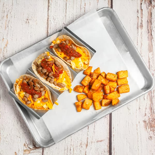 Three breakfast tacos with sausage, cheese, and salsa, served with crispy potato cubes on a tray.