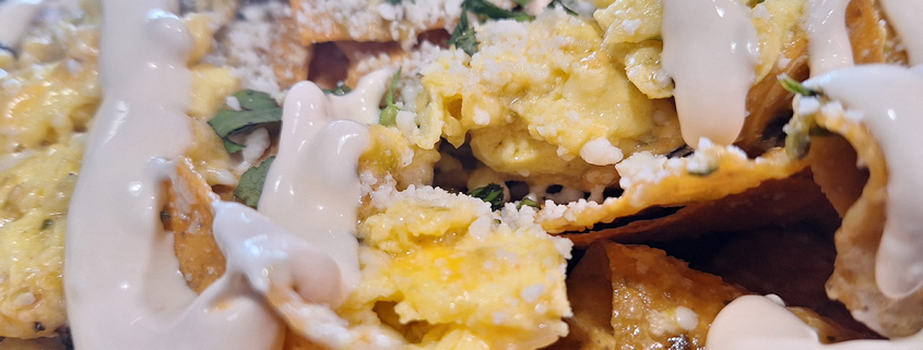 CHILAQUILES VERDE Tortilla chips simmered in tomatillo salsa with scrambled eggs & cheddar topped with cotija cheese and Mexican crema.